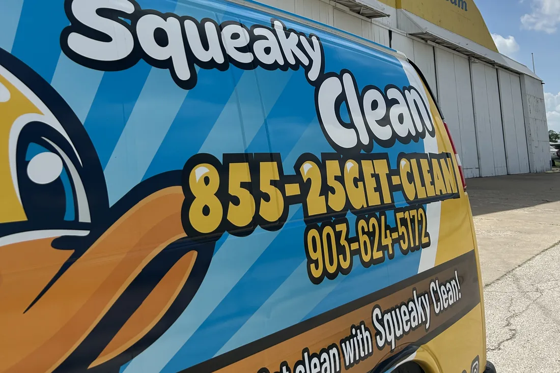 Squeaky Clean branded van, wrap showing 855-25GET-CLEAN and 903-624-5172, parked beside an aircraft hangar