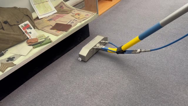 Carpet-cleaning wand working beside a glass display case of military memorabilia